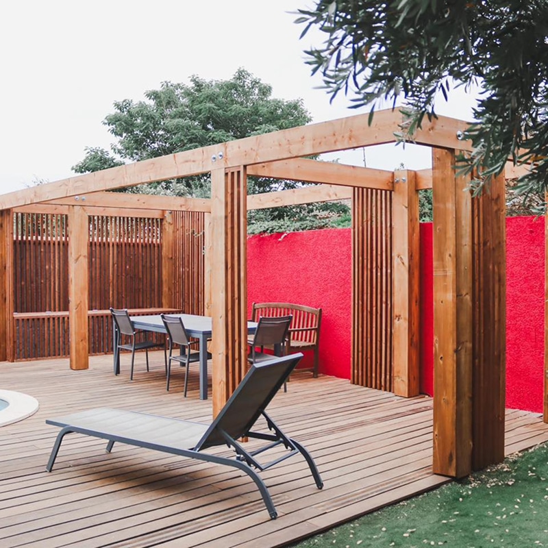 Terrasse en bois avec pergola et mur rouge vif, mobilier d'extérieur moderne, ambiance zen et design.