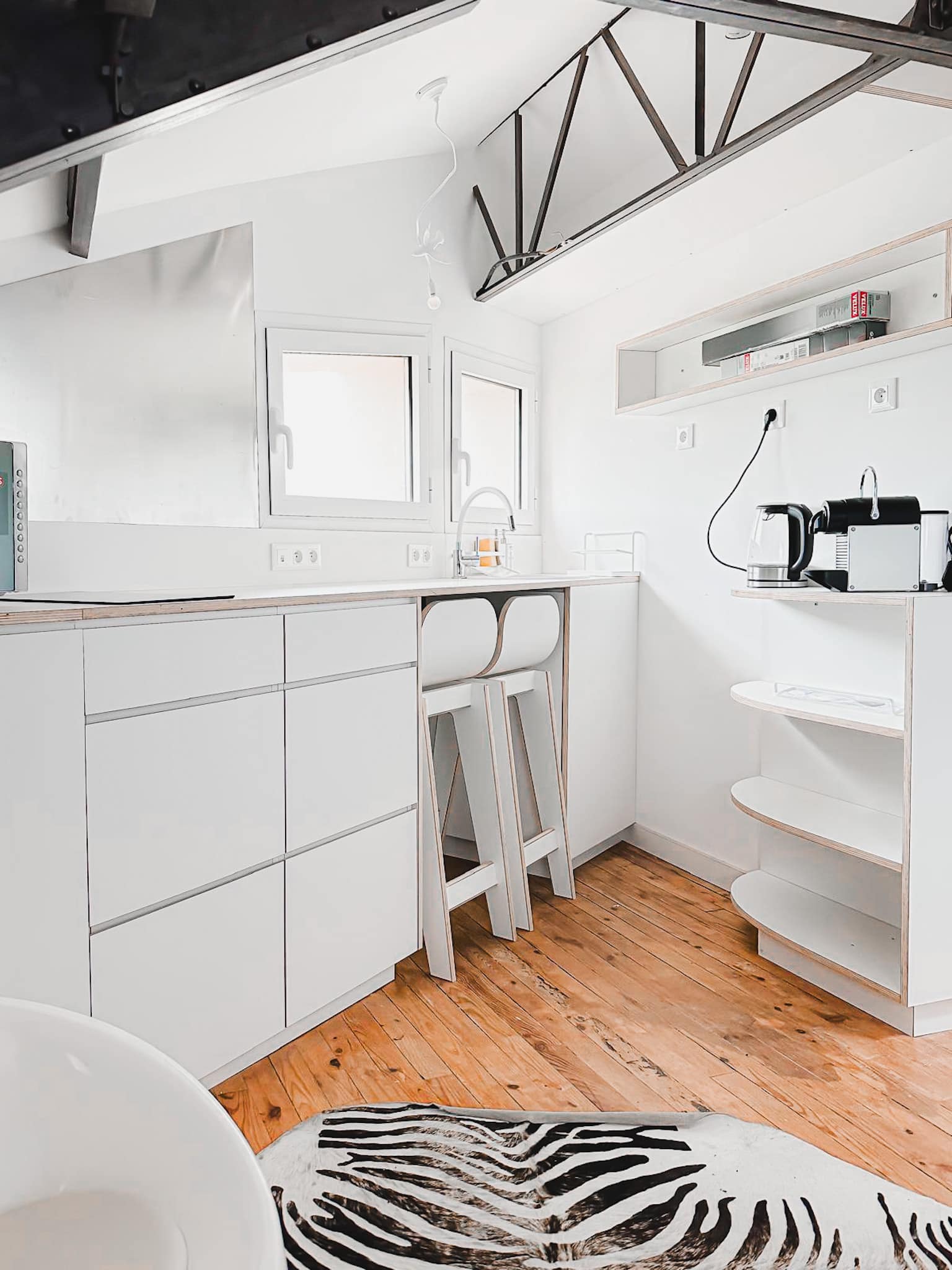Cuisine moderne blanche minimaliste avec plancher bois clair, tabourets en bois, et un tapis imitation peau de zèbre.