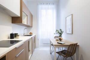 Cuisine et coin repas modernes et lumineux dans un petit espace avec armoires marron clair, plan de travail blanc, table en bois et chaises en rotin.