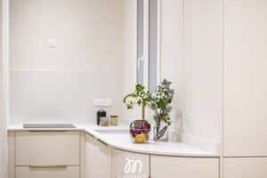 Plan rapproché cuisine moderne, mobilier beige, plan de travail blanc, robinet doré et fleurs près de la fenêtre. Logo L'Immovation.