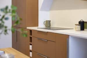 Cuisine moderne avec armoires marron chaud, plan de travail blanc, plaques de cuisson noires et bocaux de céréales sur le comptoir.