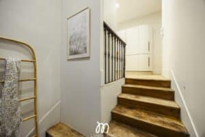 Escalier rustique avec marches en bois patiné, rambarde noire et murs blancs. Cadre photo déco et porte-serviettes en bambou.