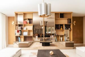 Bibliothèque en bois clair avec miroir central et lustre moderne dans un salon lumineux.